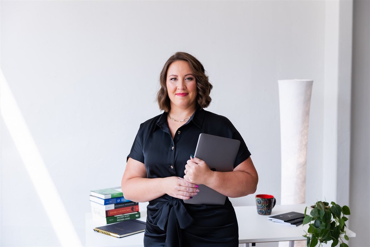 Trauma and wellness coach, Kathryn Konicek, holding her laptop in her office
