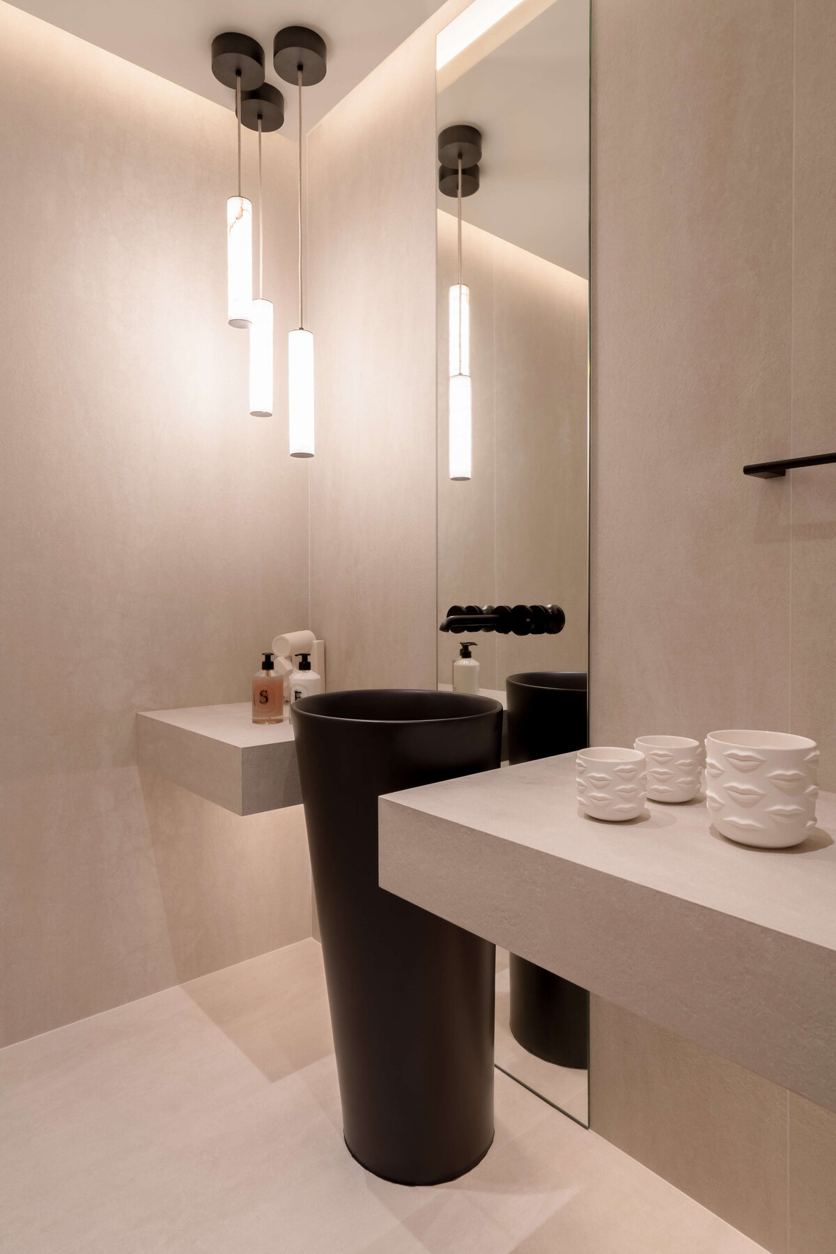 Modern bathroom featuring a light, airy aesthetic contrasted by a dramatic black pedestal sink, Three cylindrical pendant lights emit a warm glow.