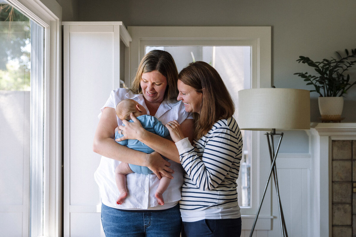 two moms holding and looking at newborn in blue onesie