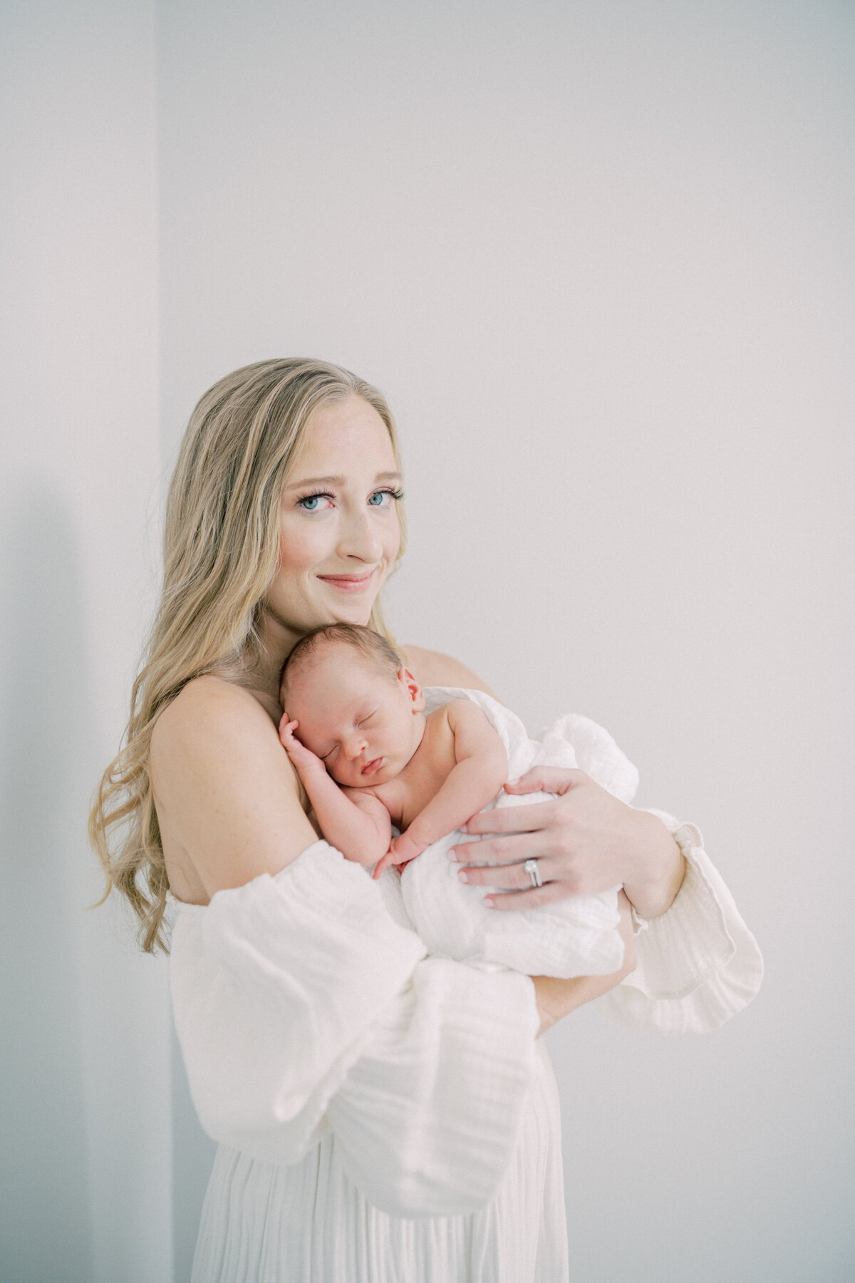 Blonde mother holds her newborn baby up to her chest as he sleeps peacefully