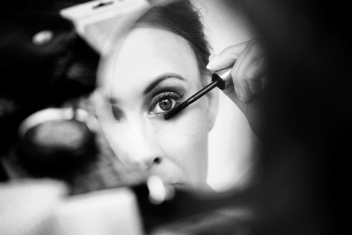 A favourite wedding photo in black and white of a bride close up putting mascara on in the mirror. The photo is the reflection in the mirror taken at an amazing wide aperture of f1.2 on a 50mm lens