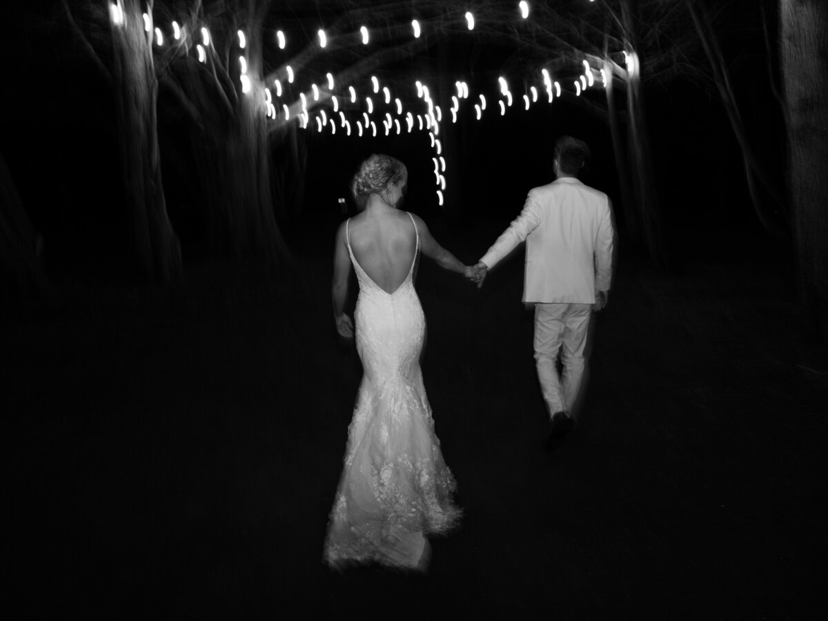 Bride and groom holding hands at wedding reception with market lights hanging above