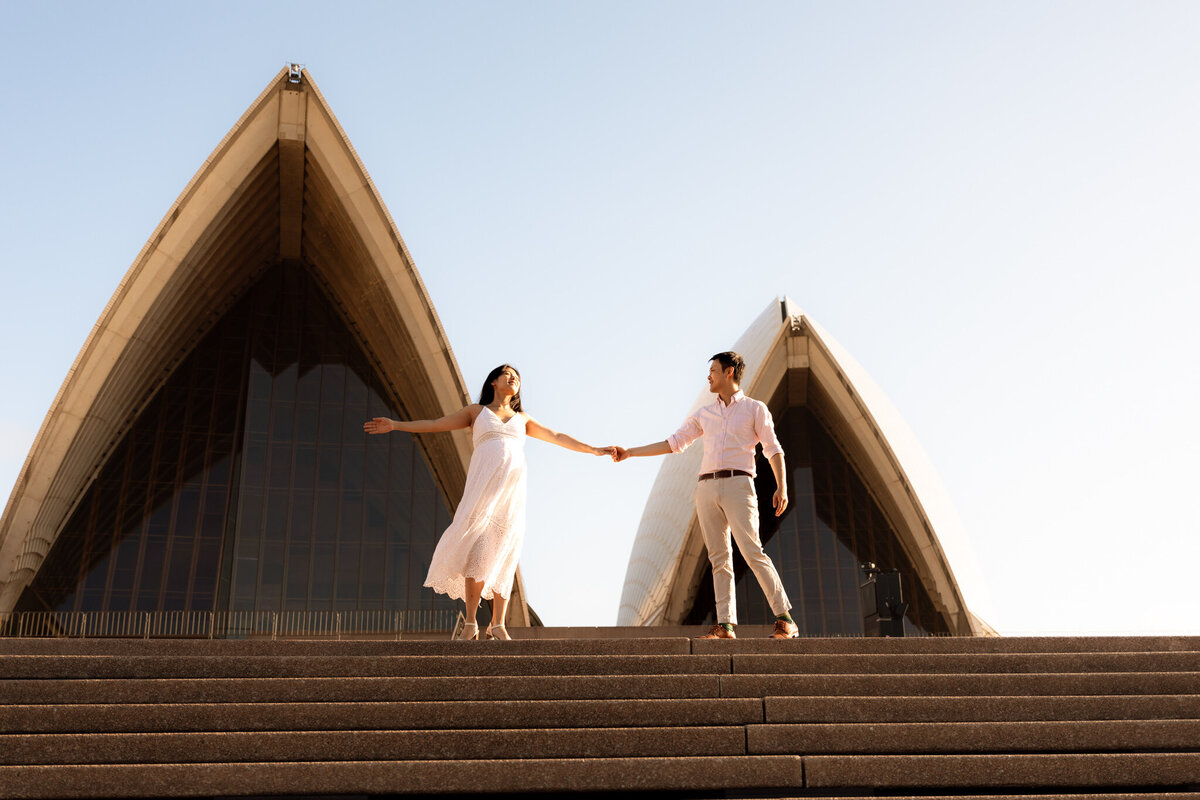 Pregnant couple holding hands in front of the Sydney Opera House during a golden hour maternity photoshoot