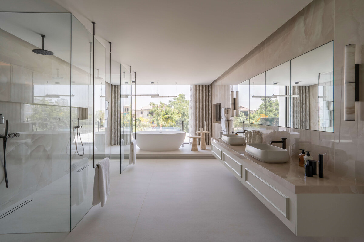 Spacious, modern primary bathroom with a double sink to the right, a large, glass walk-in shower to the right, and a large soaking top against the far wall.