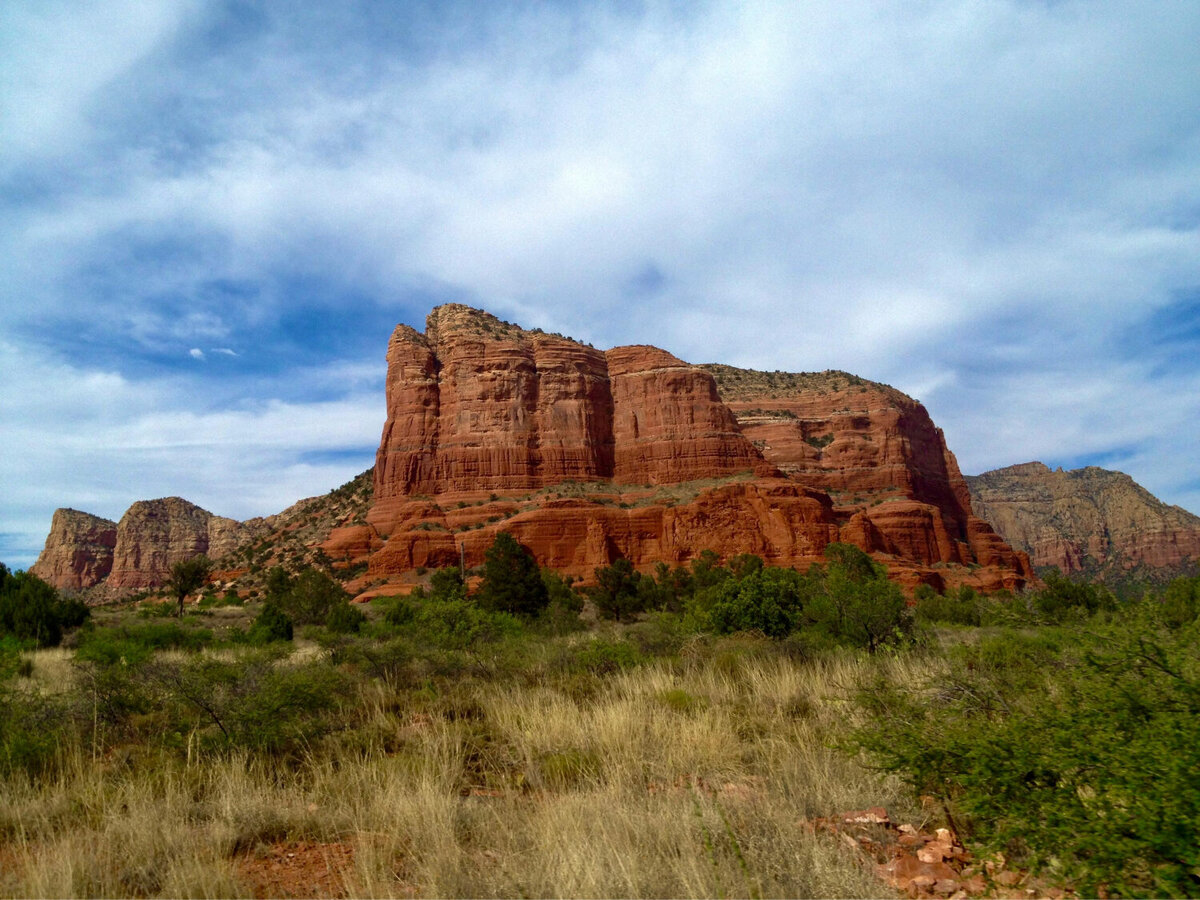 Red rock sedimentary rock structures with lush green grass and greenery in front of them.