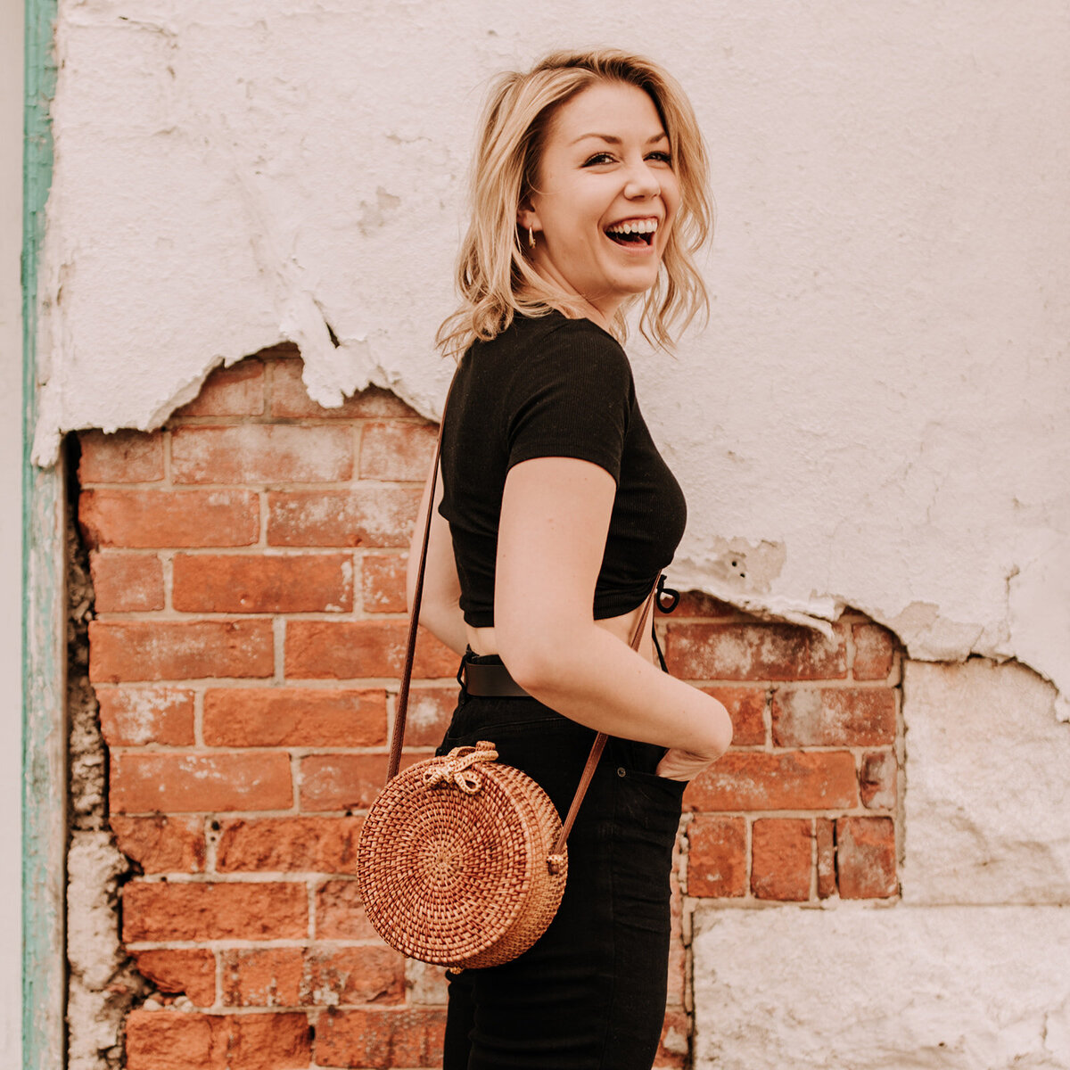 A woman laughs while standing in front of a brick wall.