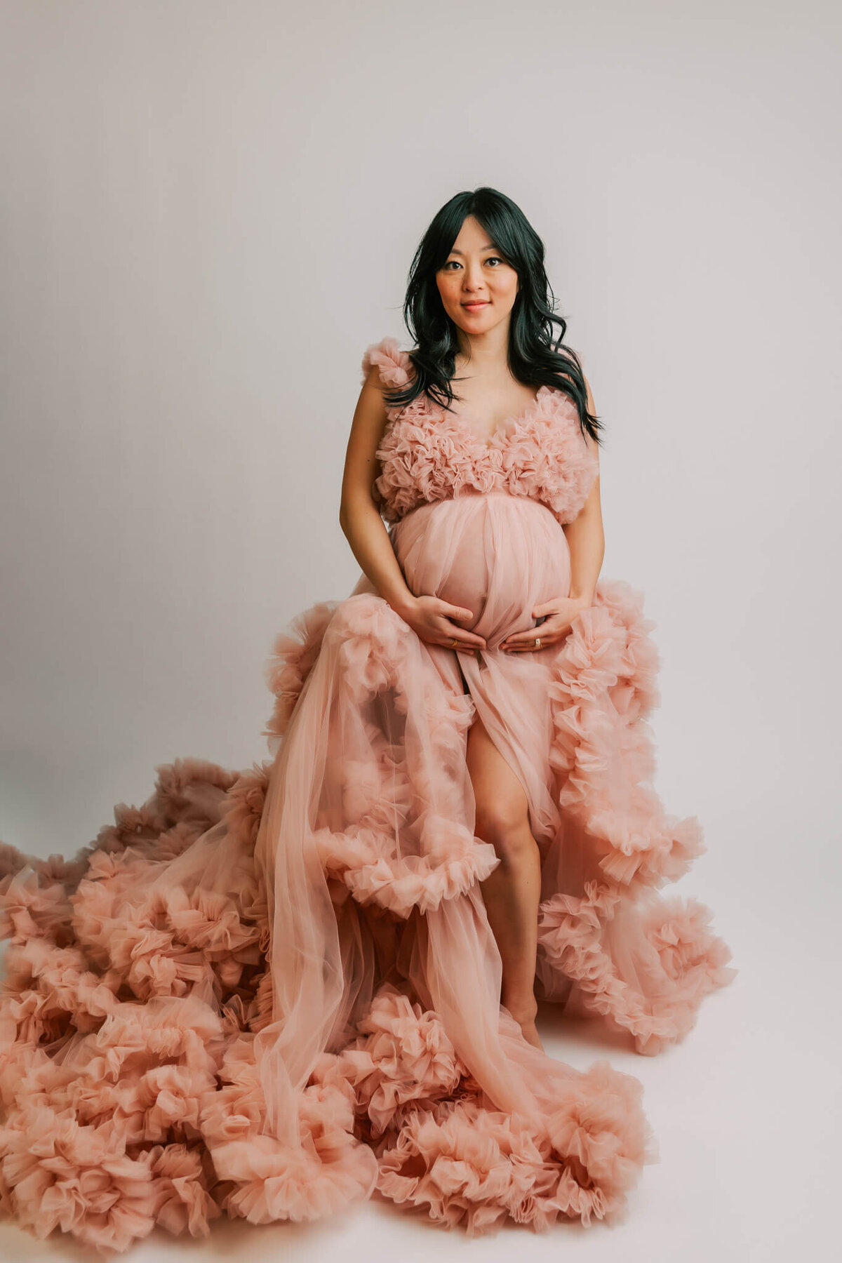 standing pregnant woman in pink tulle gown. she is looking at the camera and smiling
