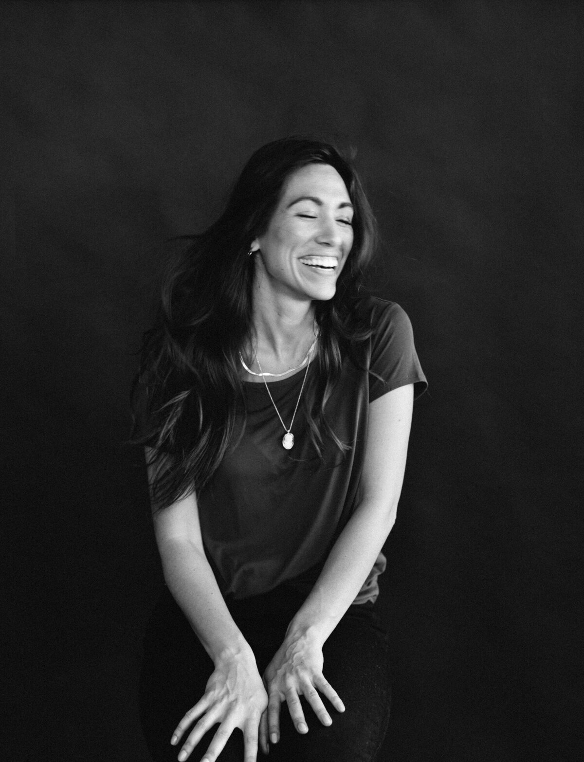 woman with dark hair laughs, hair movement, black studio backdrop