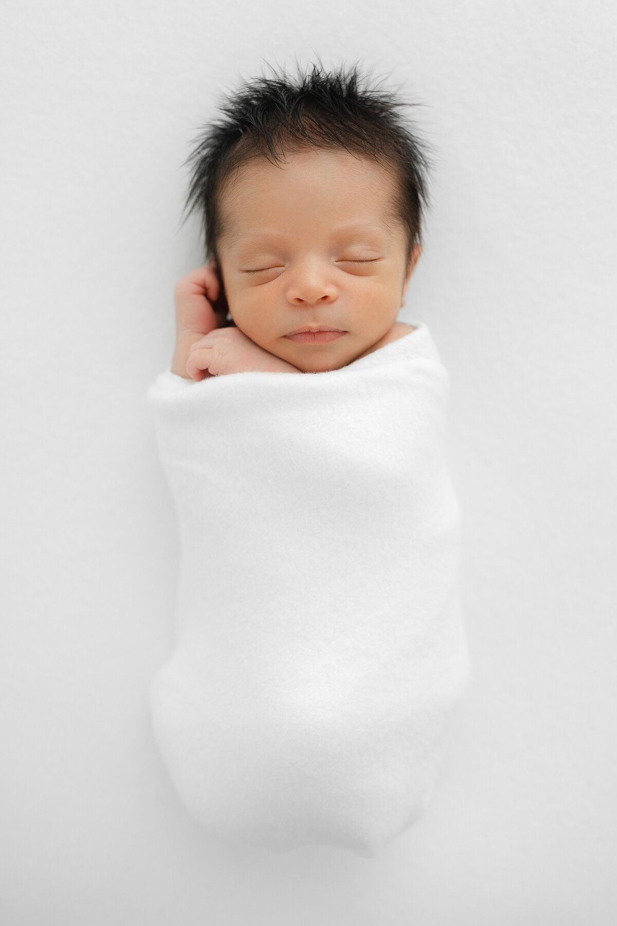 A Nova Studio Photography  newborn photo of a newborn baby sleeping in white swaddle on a white blanket