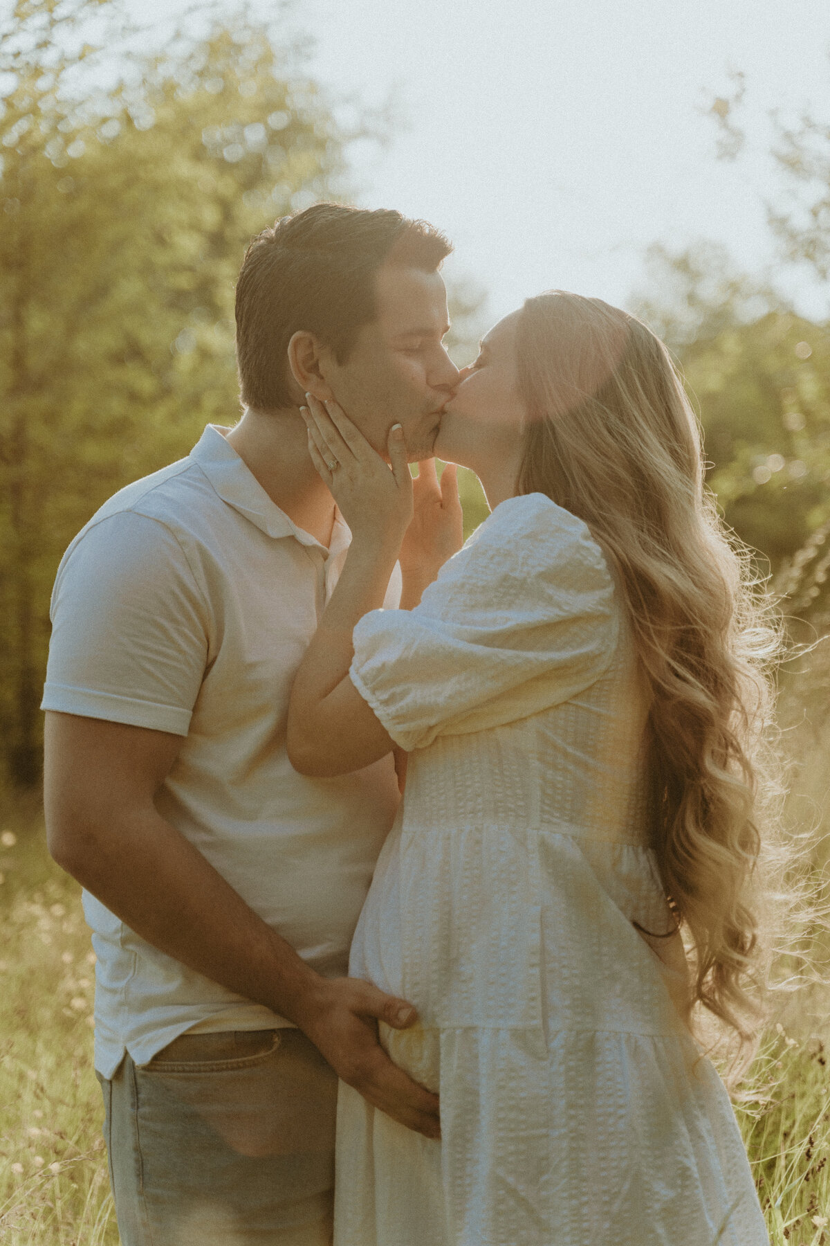golden hour maternity photo of a husband and pregnant wife kissing in a field