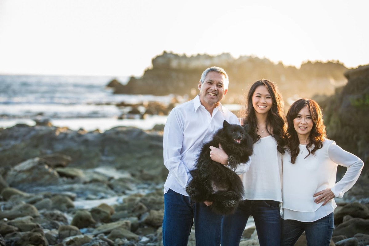 Family poses for photo with their dog on the rocks along the beach in Laguna