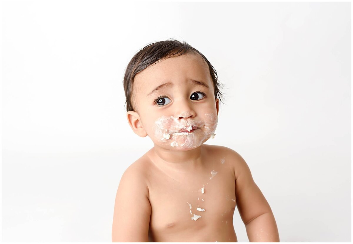 Toddler with cake frosting on his face at cake smash session.