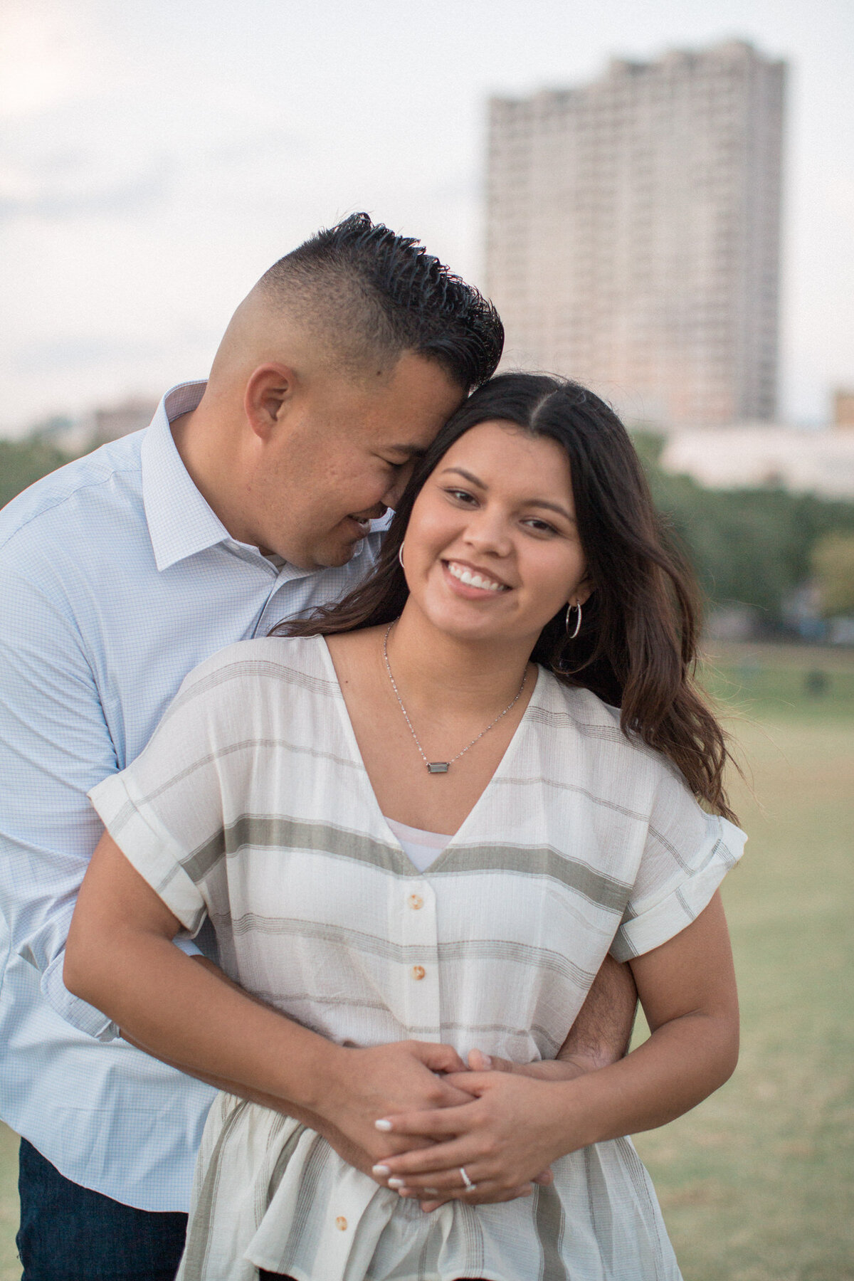 A man snuggles close to his new fiancee with a city skyline view.