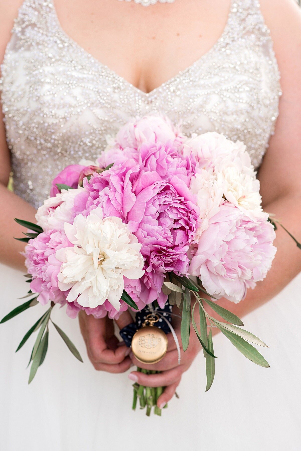 bride wearing a wedding dress with a beaded bodice and tulle skirt holding a small bouquet of pink peonies and white peonies with hints of greenery and an engraved gold pocket watch.