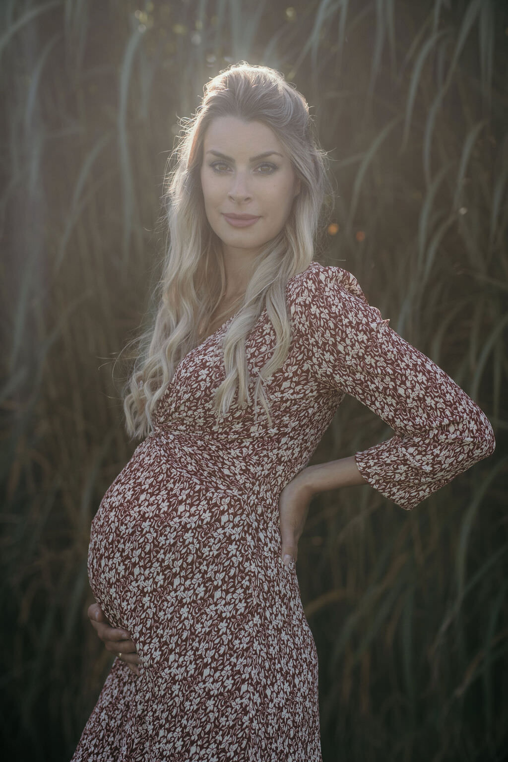Pregnant woman stands in the soft sunlight.