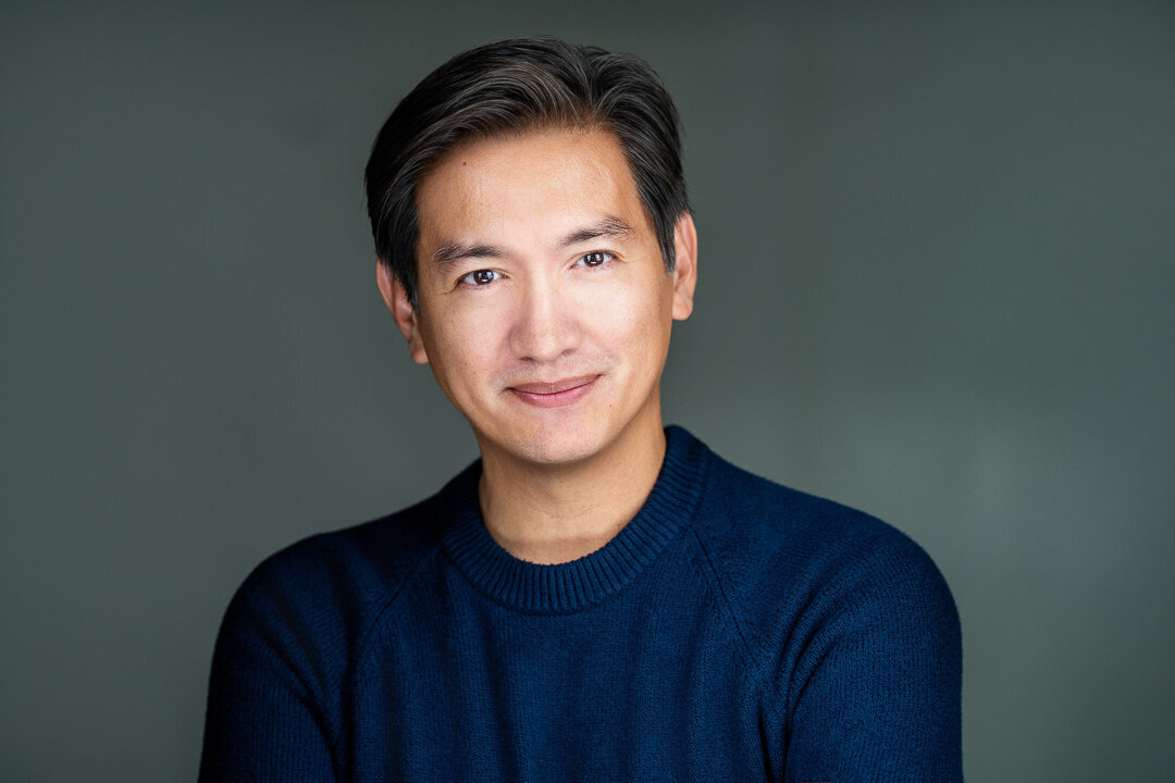 Professional branding headshot of a man wearing a navy sweater against a soft gray background, captured in New Jersey by Alex Kaplan Photography.