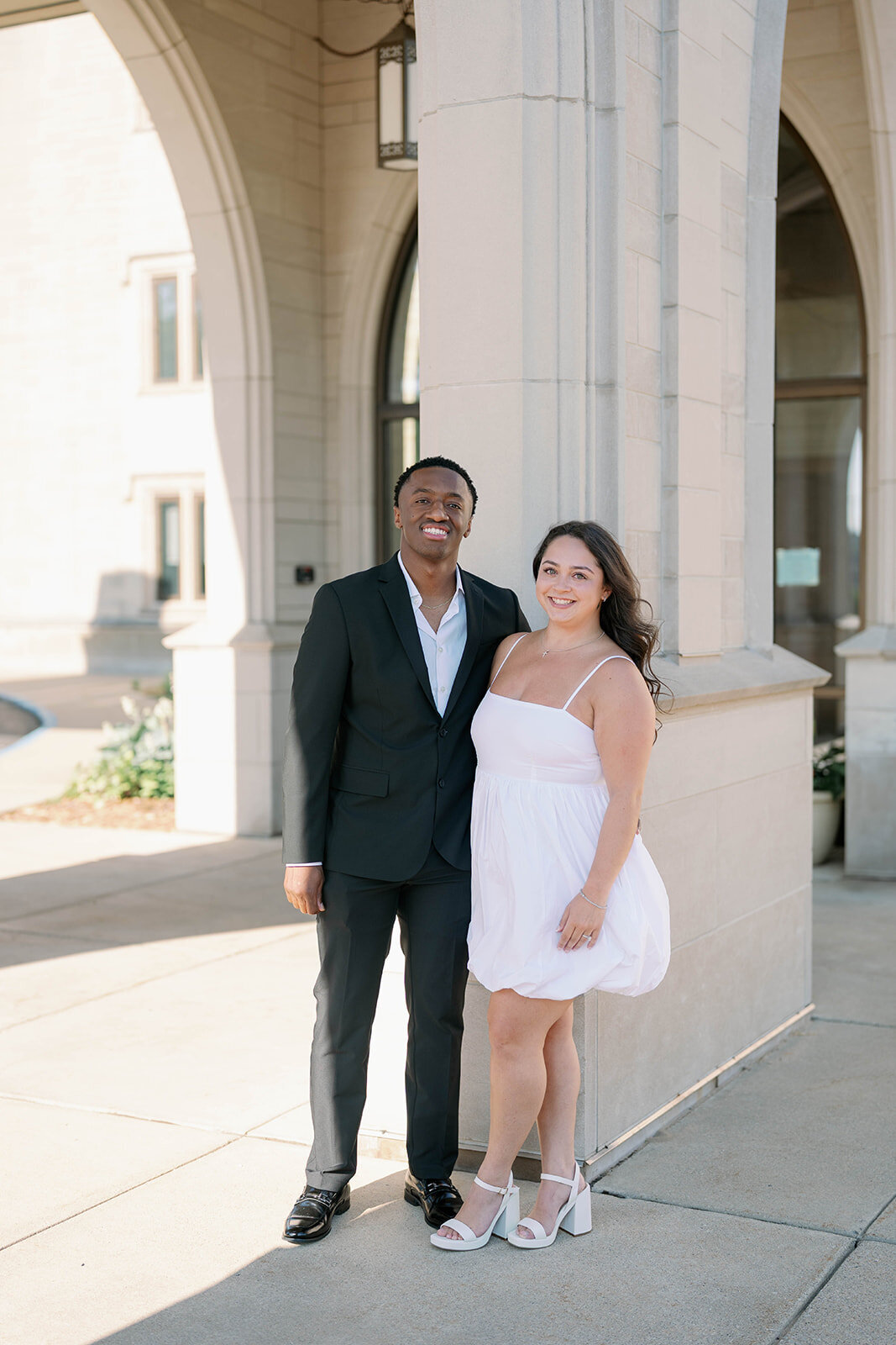 Engaged couple standing together under stone archway during their downtown Kalamazoo engagement session.