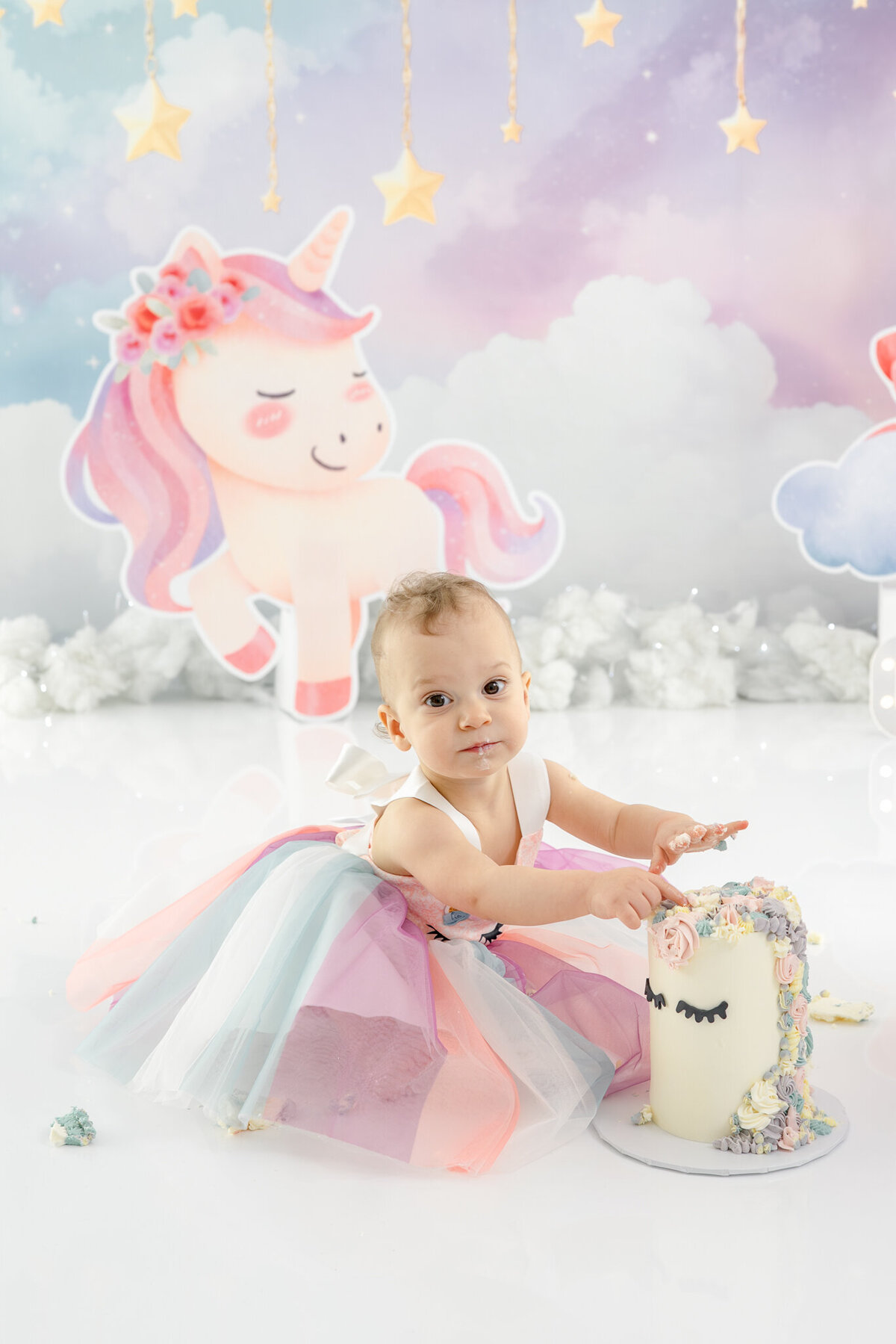 Girl in unicorn dress eating unicorn cake during themed cake smash session— captured by Alliston and Barrie cake smash photographer.