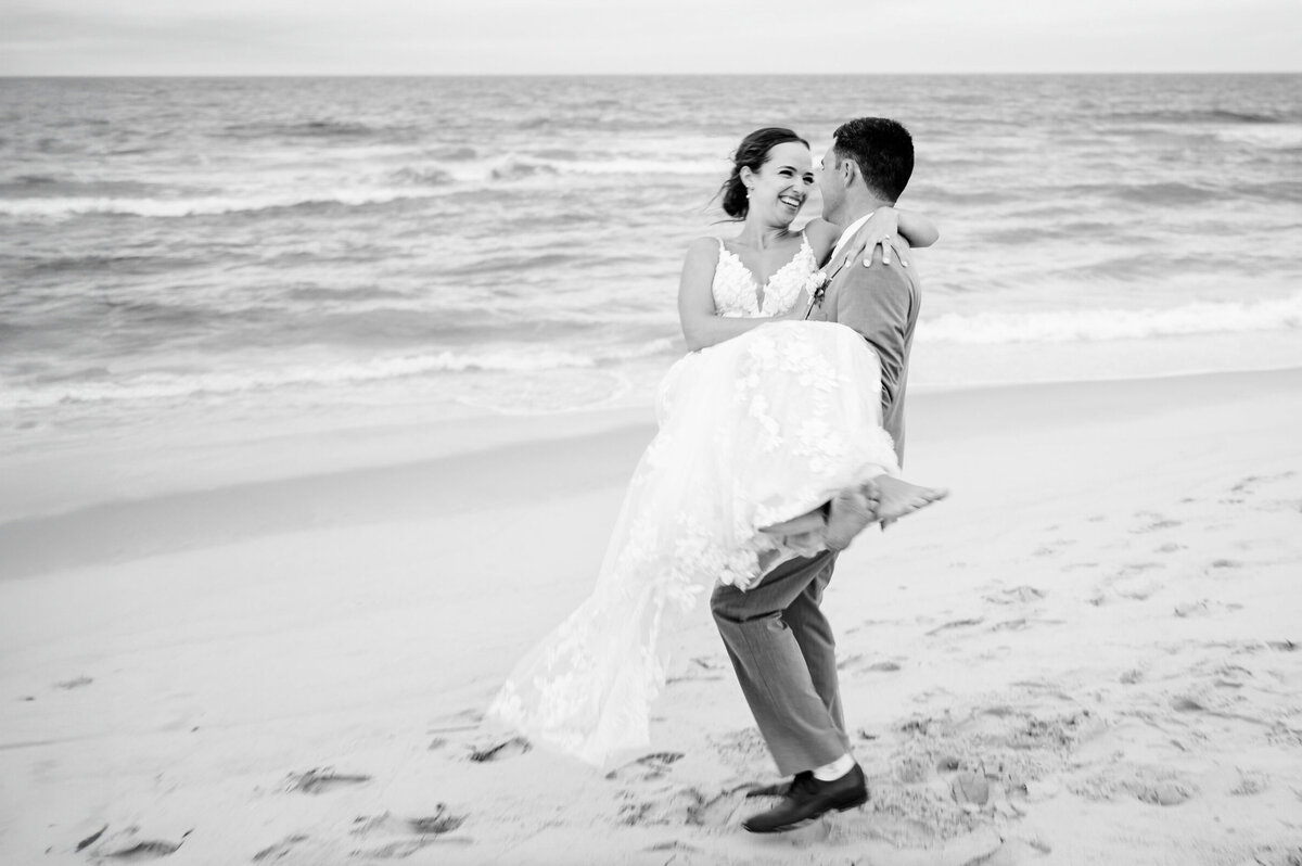 Groom carrying and spinning his bride around on the beach outside of seashell resort in Beach Haven, New Jersey