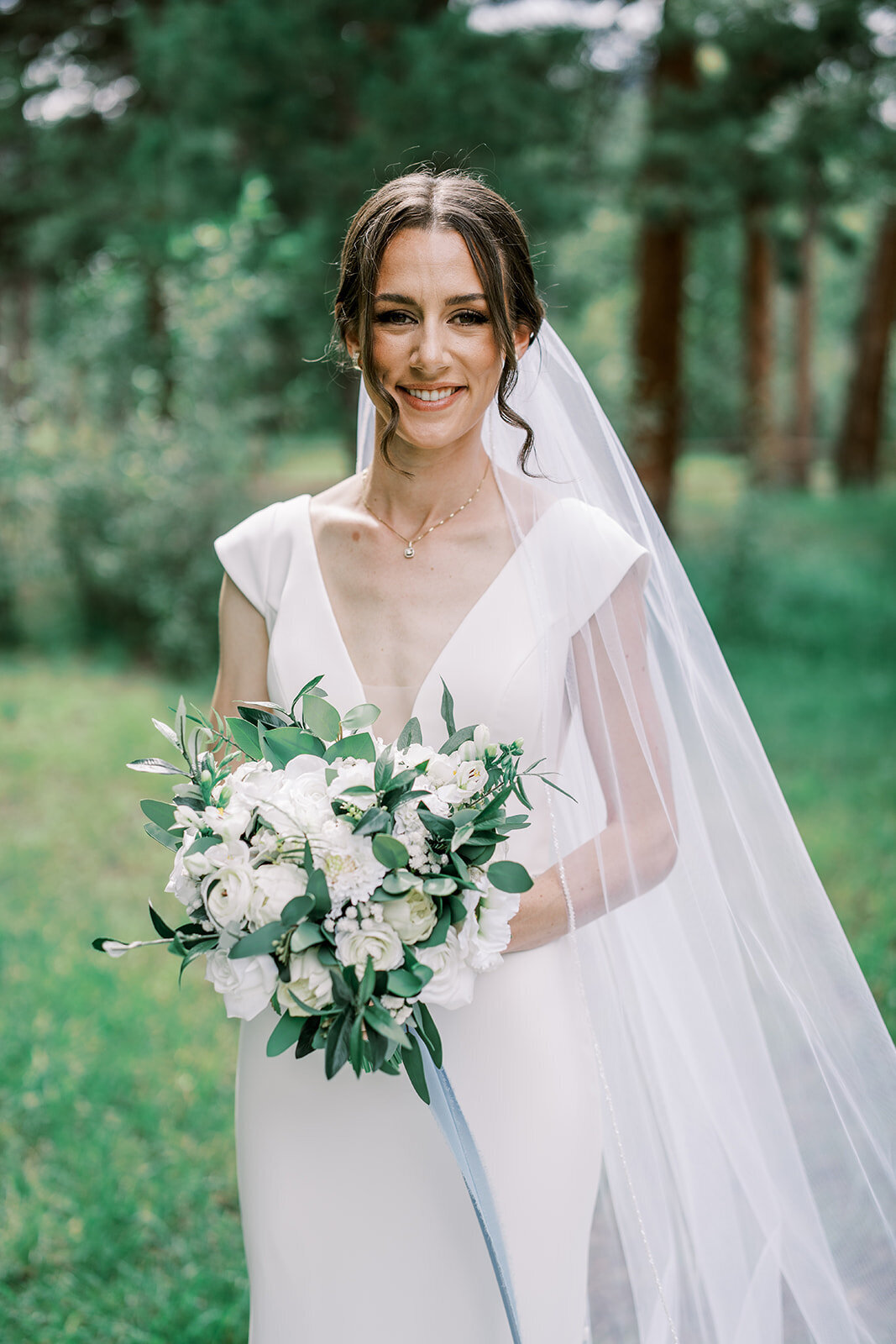 Bride smiles before her wedding ceremony with a white lush floral bouquet with greenery at the Landing at Estes Park.