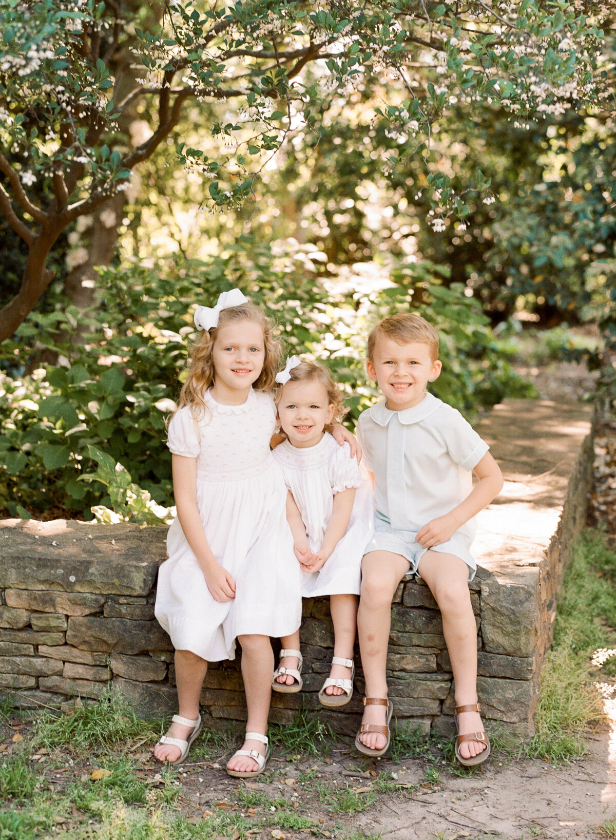 Three siblings smile at the camera for a portrait at the Raulston Arboretum. Image by Raleigh maternity photographer A.J. Dunlap Photography.
