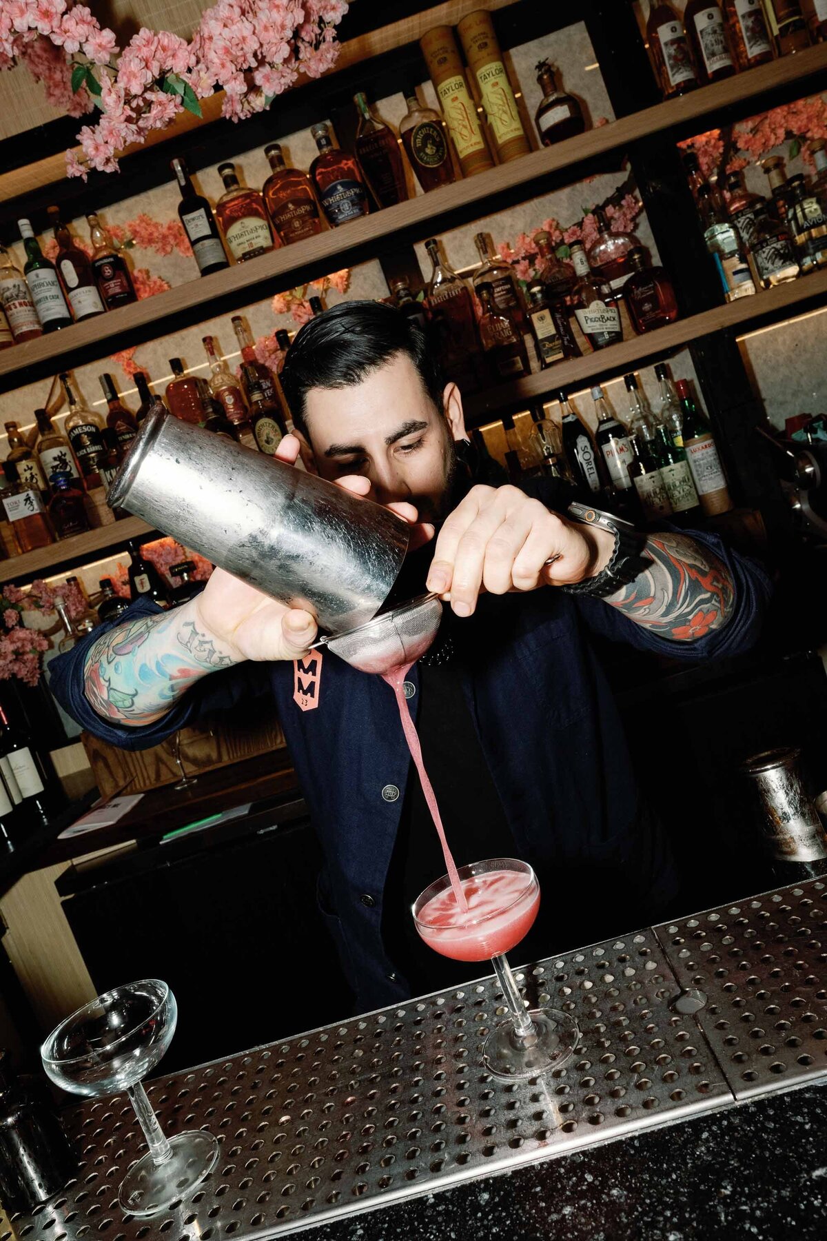bartender makes pink cocktail for cherry blossom floral install at mercy me bar rehearsal dinner in washington dc wedding