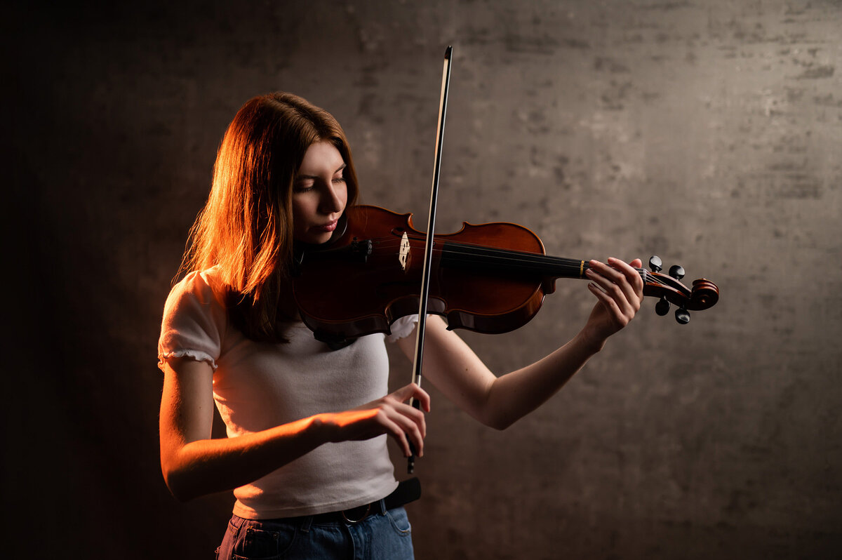 A young lady from Waukesha North High School plays her violin in our Waukesha studio while her senior portrait is taken.