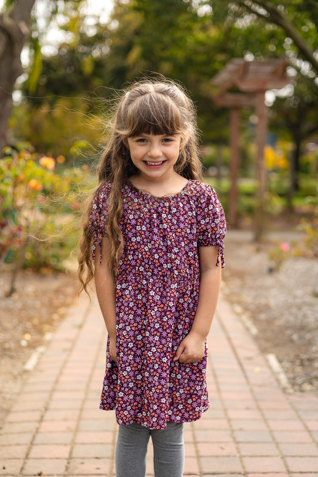 Girl wearing floral dress in rose garden smiling during Bay Area school photography lifestyle portrait – Ellobelle Photography