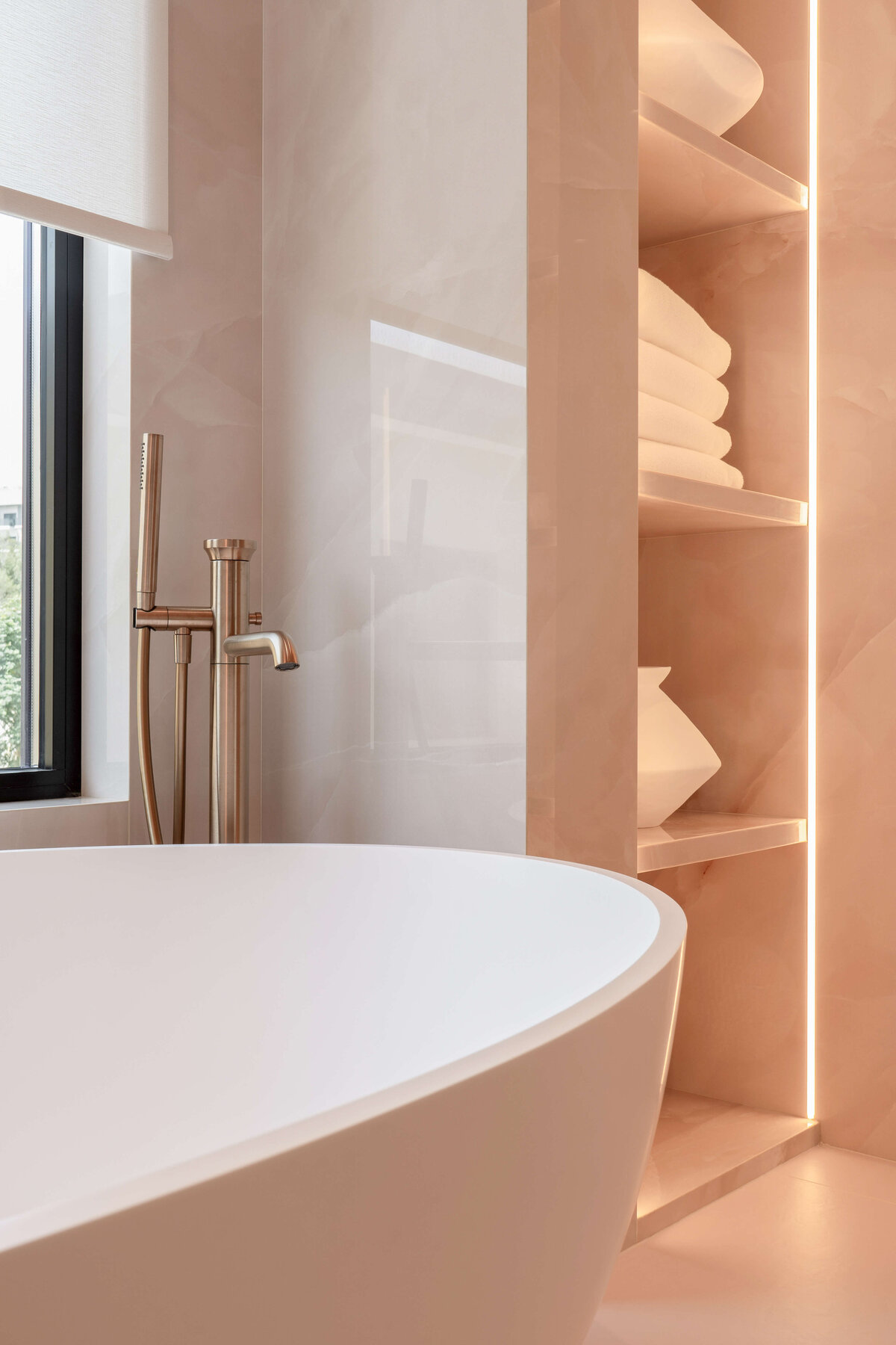 Large white soaking tub with a rose gold spout in a light pink marble bathroom.