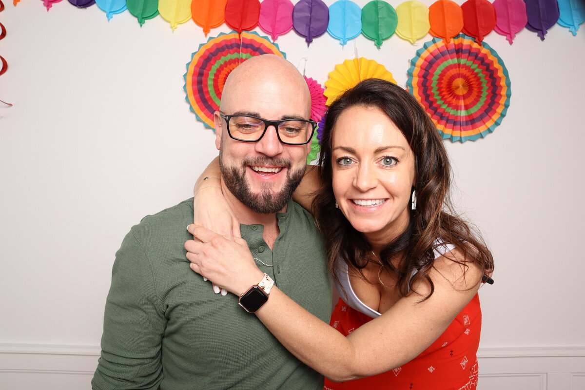 brother and sister smile at camera with colorful garland in background