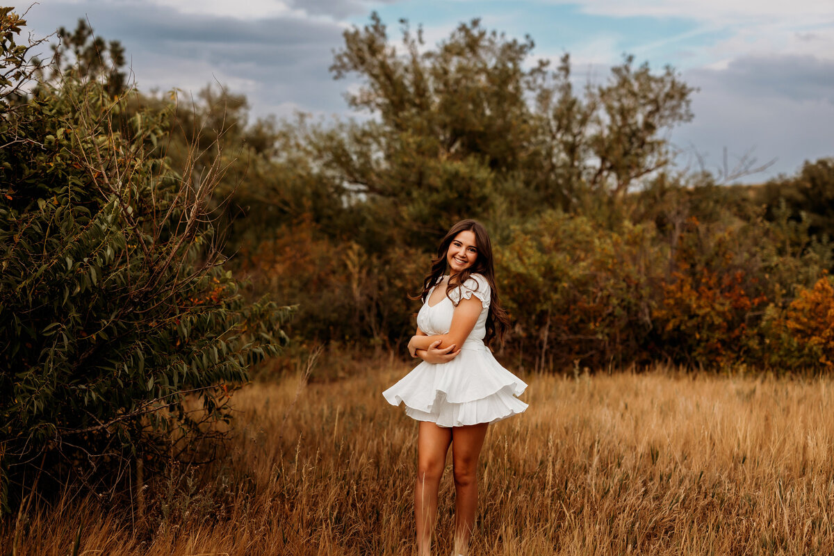 Teenage girl twirls her white dress in the middle of a tall grassy field in Boulder Colorado for her senior portraits