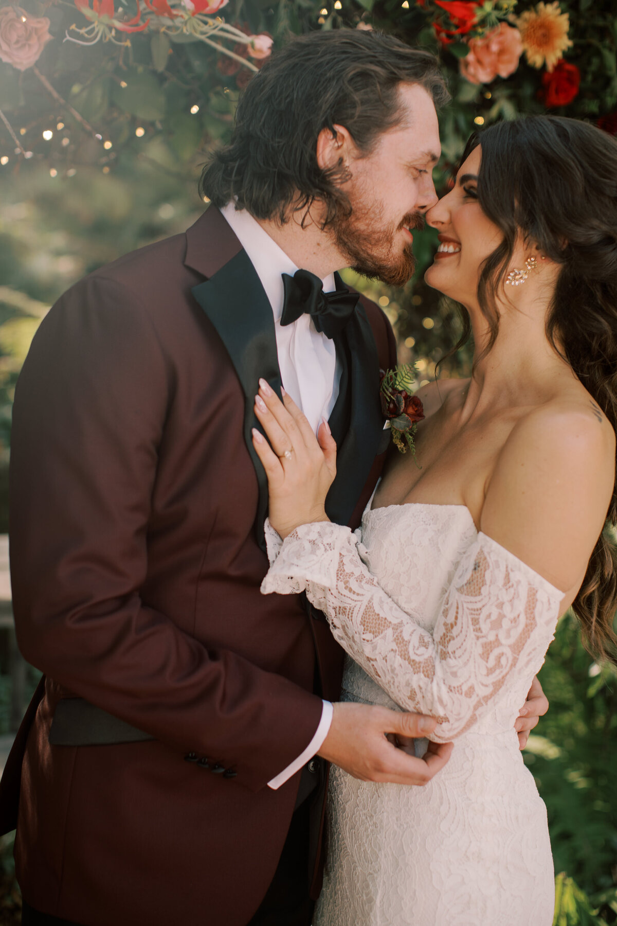 bride and groom timeless photo kissing while bride in a timeless wedding dress and groom in a maroon tux