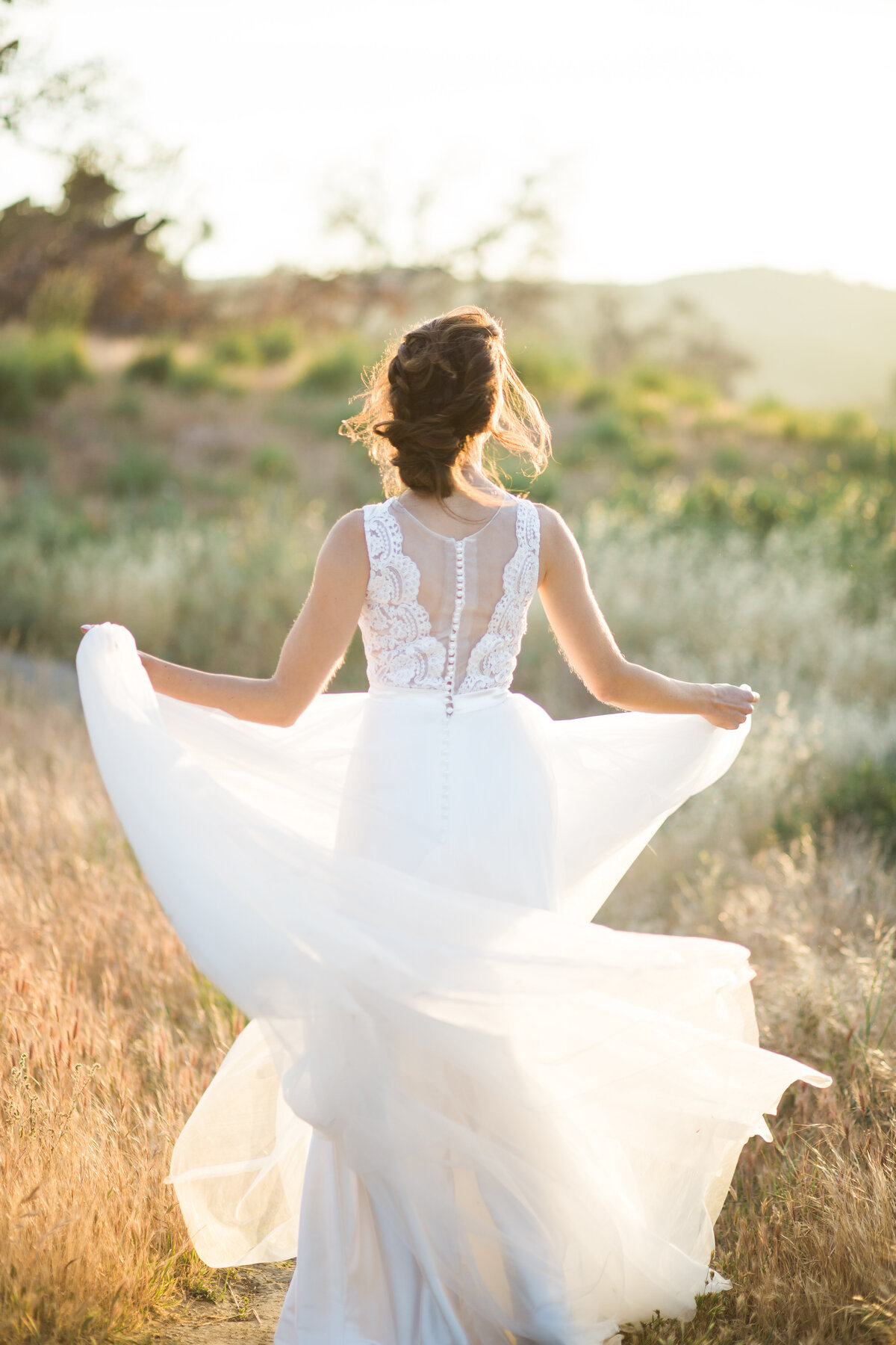 Bride swirls her wedding gown skirt as she walks through a field
