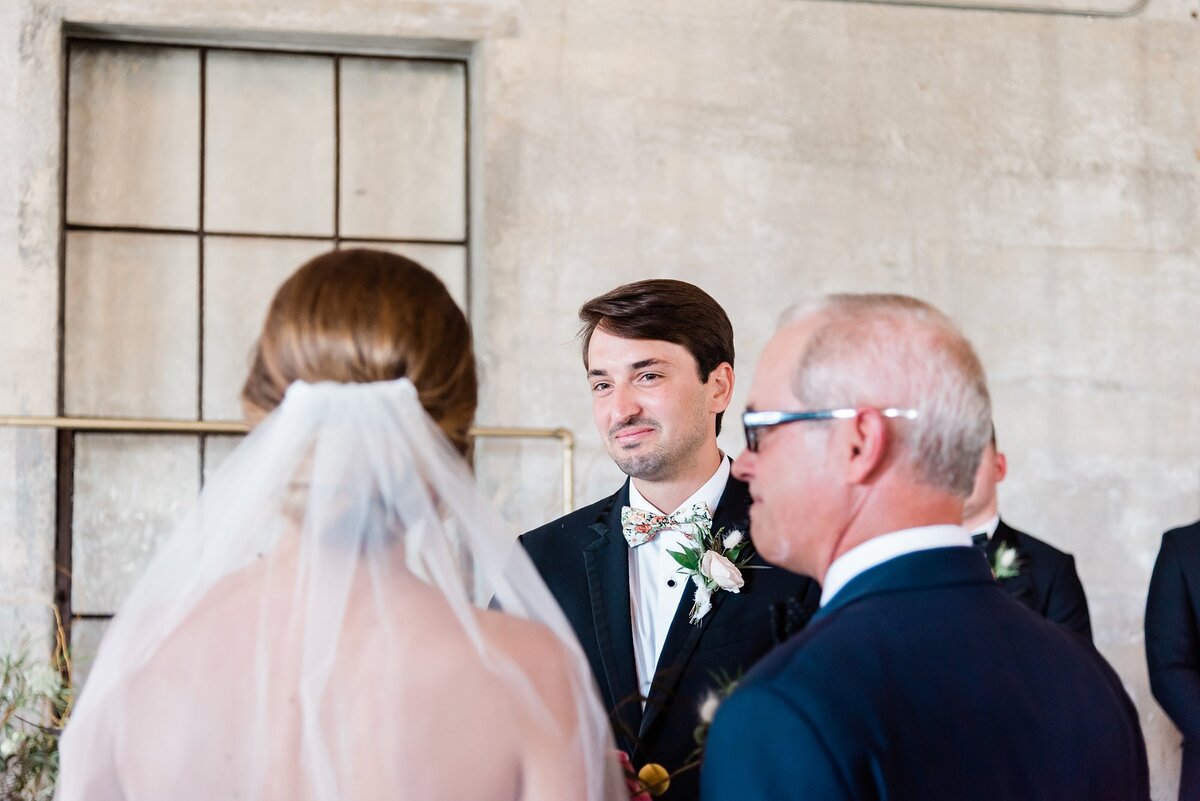 Groom smiling at bride after she just walked down the aisle and is waiting to be given away by her father at Olde Dobbin Station