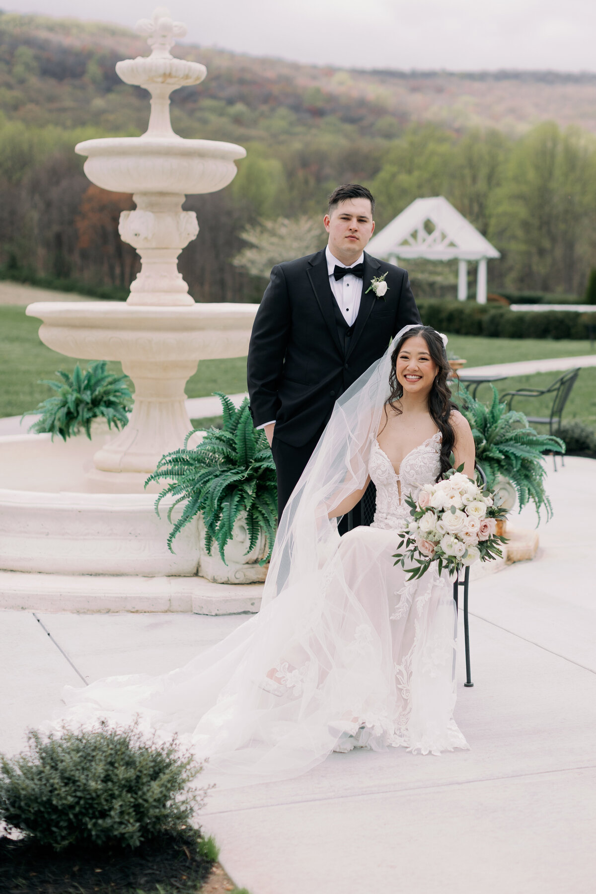 Bride wearing lace gown from Posh Bridal holding bouquet at Springfield Manor outdoor ceremony.