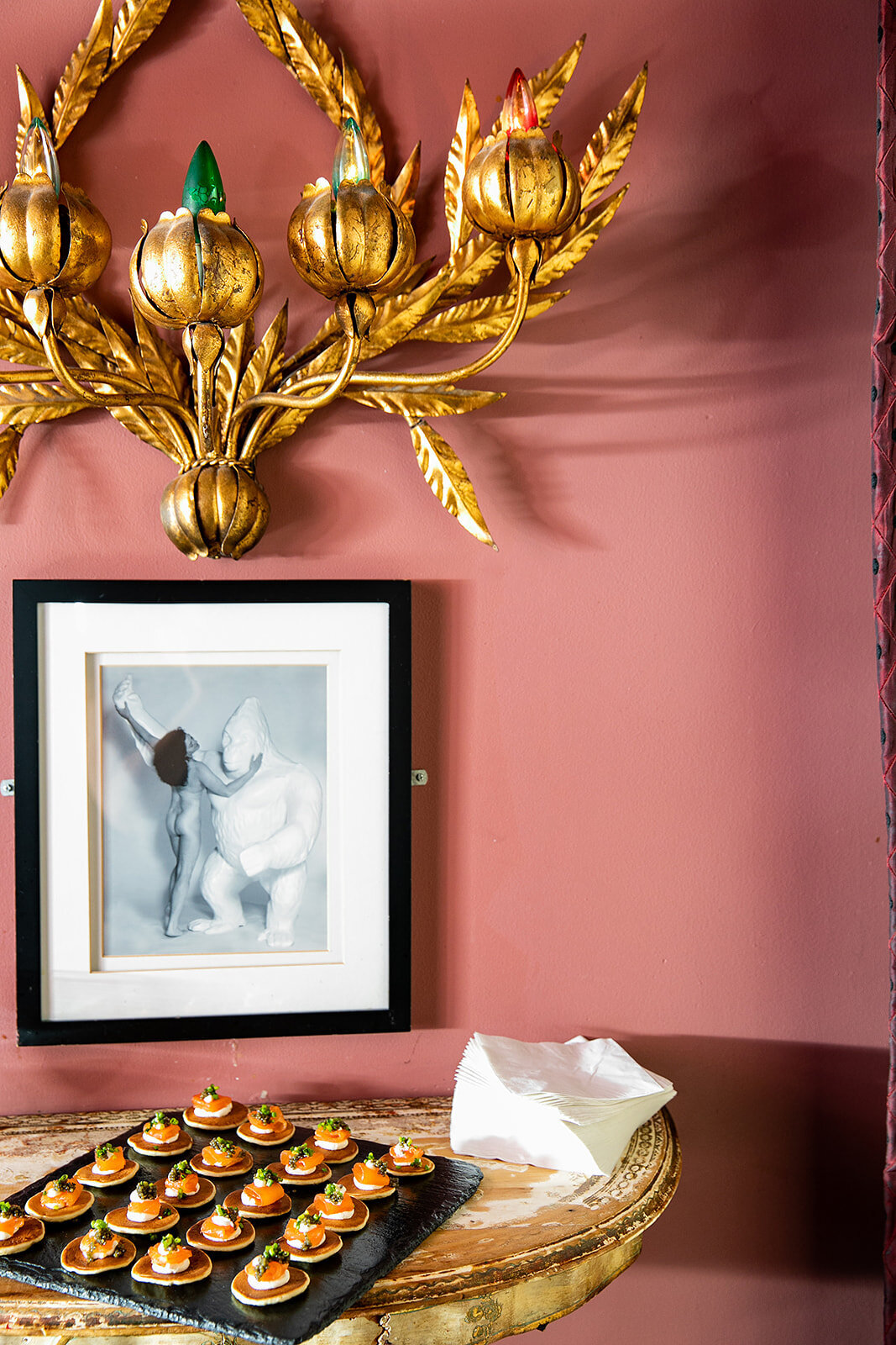 Elegant tray of canapés displayed on a side table beneath a gold wall sconce and framed artwork at Norwood in New York.