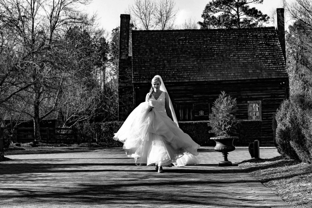 A bride holding her dress and walking along a driveway