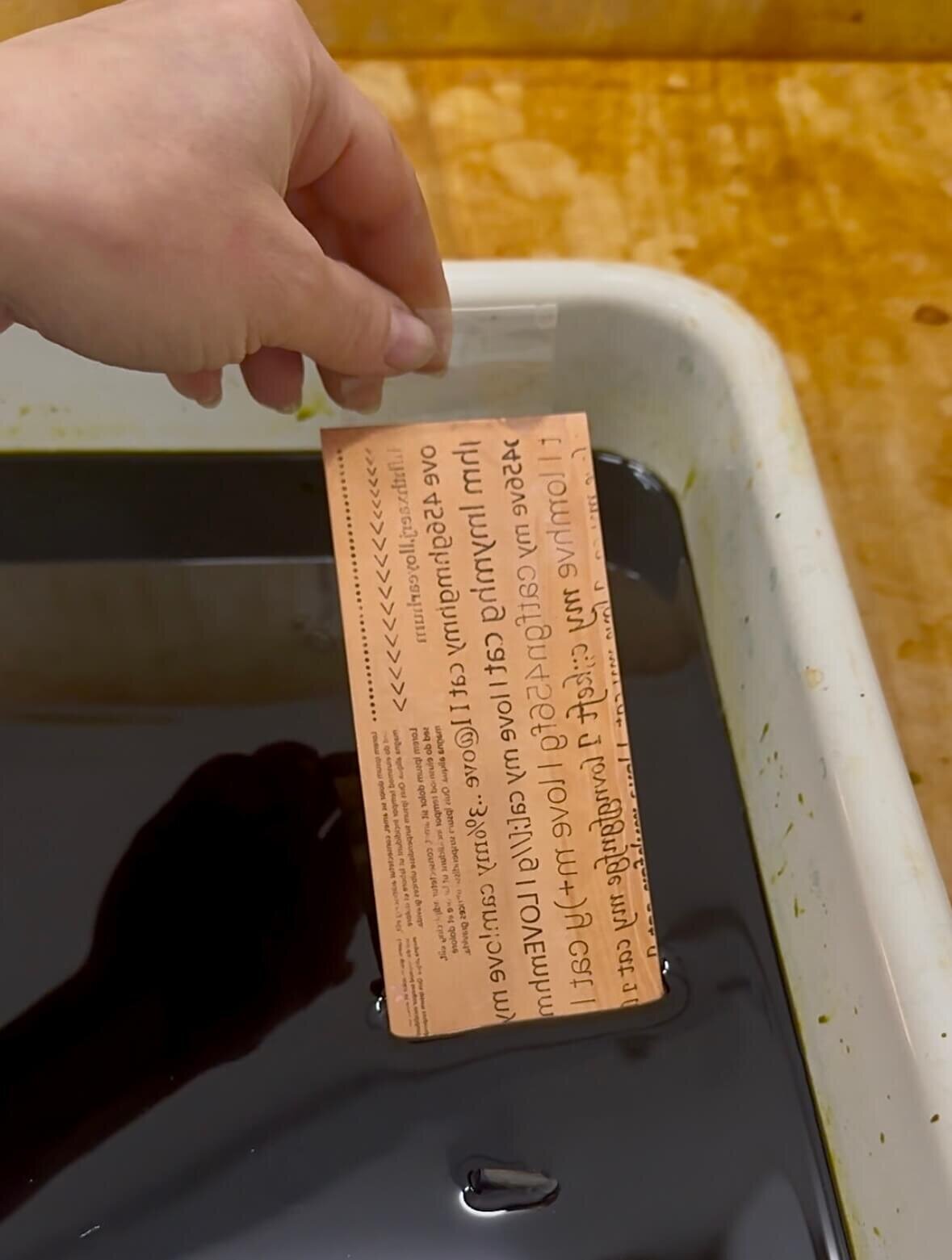 A copper plate with reversed text being lifted from an etching bath, part of a toner transfer experiment.