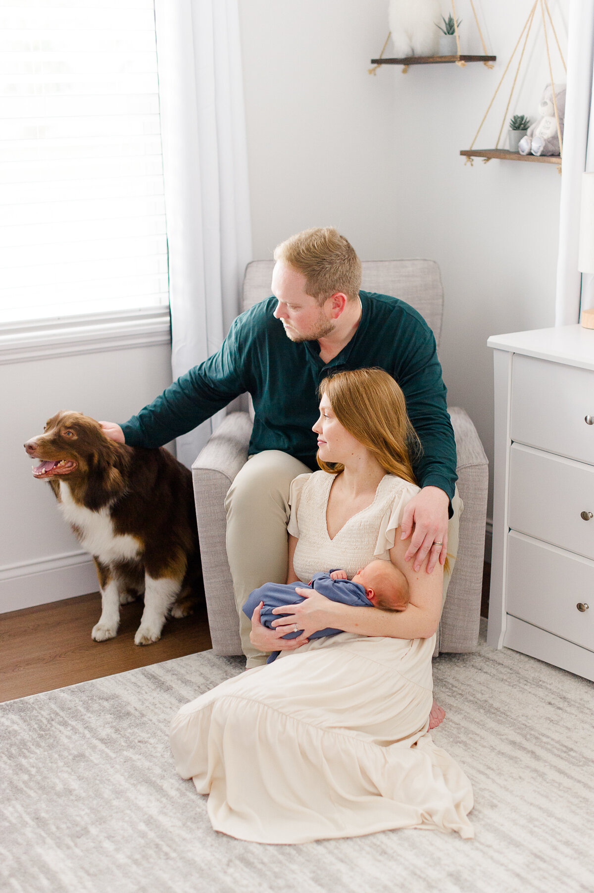 Young couple holds newborn baby in his room while petting their dog