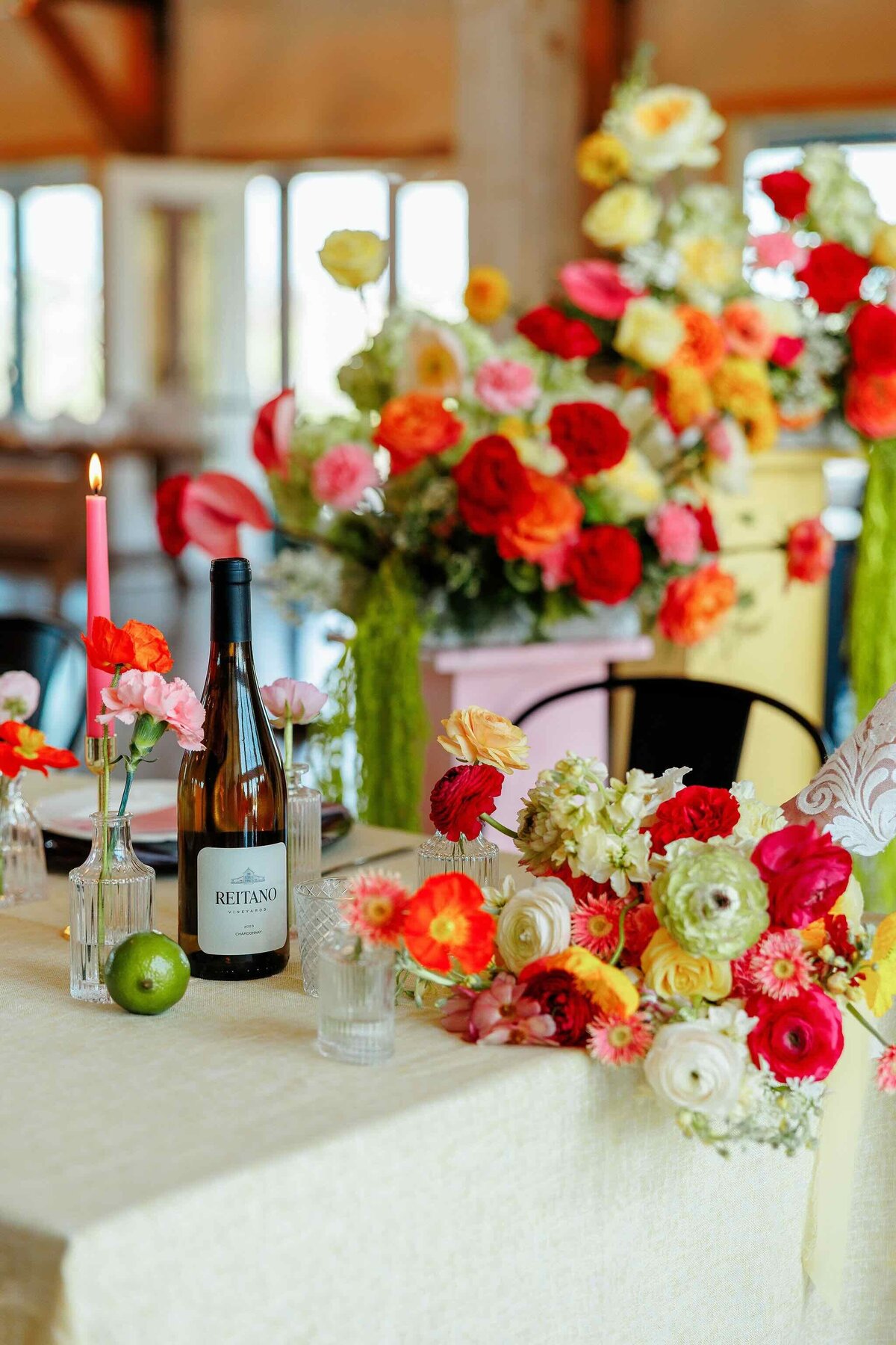 Wedding reception table styled with citrus, champagne, and vibrant florals in a modern barn venue.