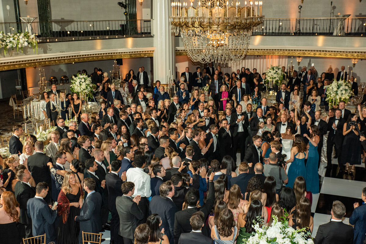 A large crowd of people are gathered in a room with a chandelier