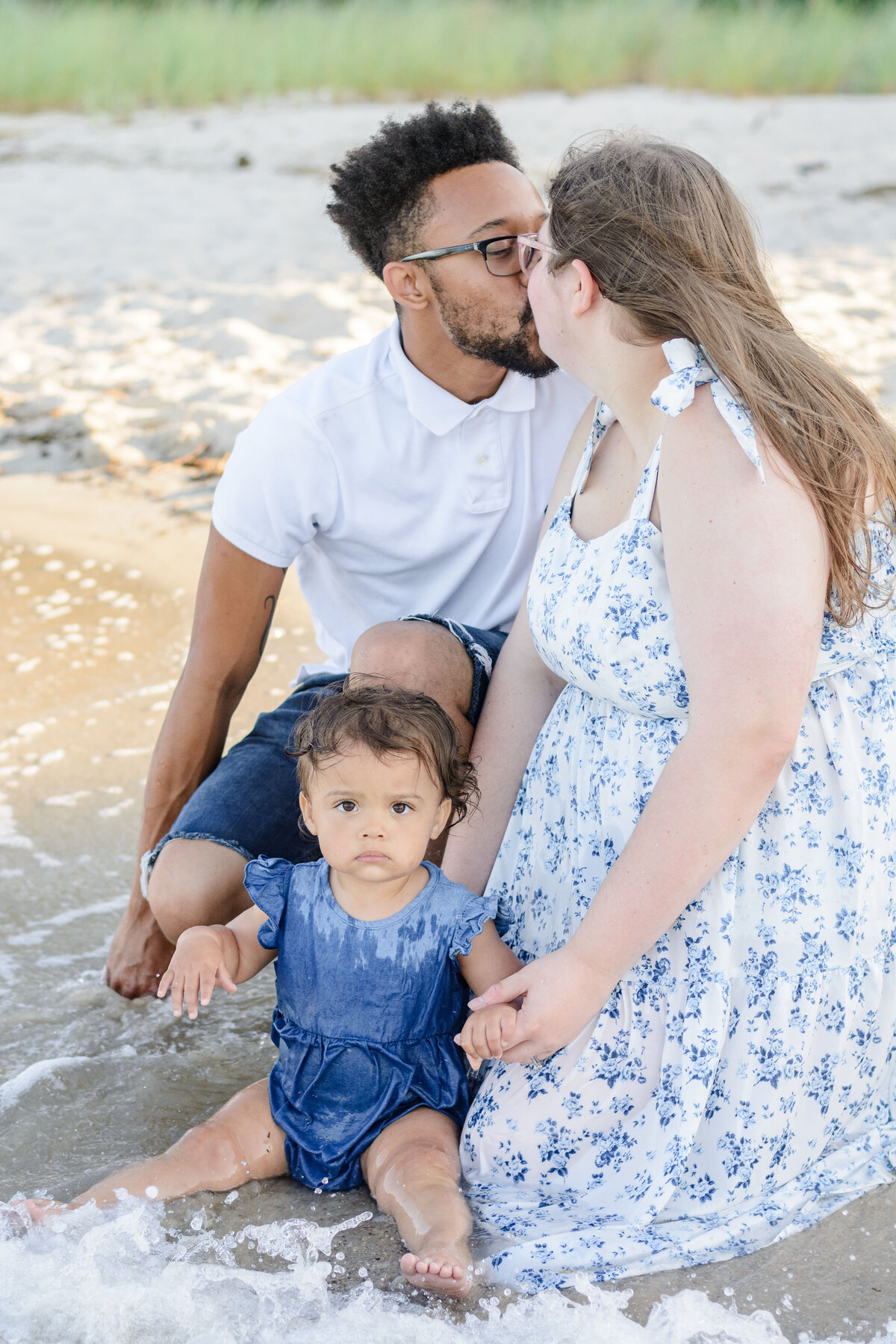 Mother and father sharing a kiss while their baby splashes