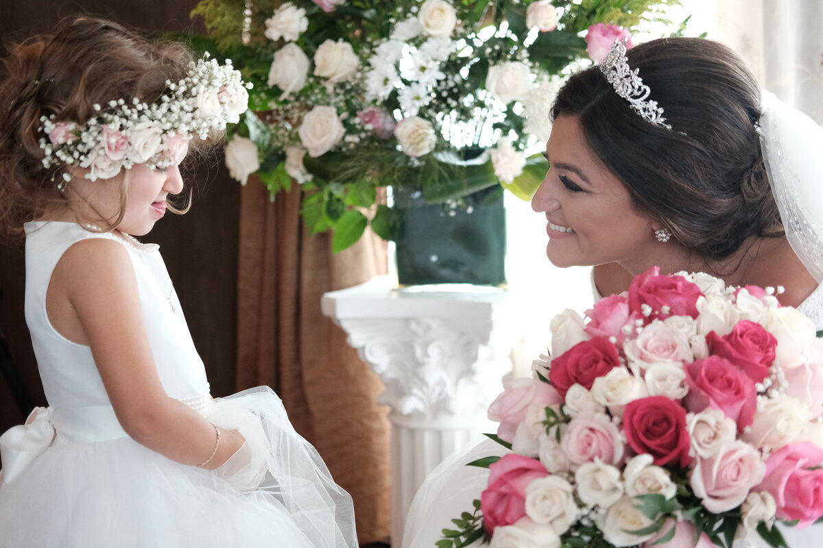 A bride shares a joyful and affectionate moment with a flower girl, capturing their bond and the playful, heartwarming aspect of the wedding day. This image highlights the bride’s elegance and the charm of the flower girl, adding a personal and endearing touch to the bridal portrait gallery.