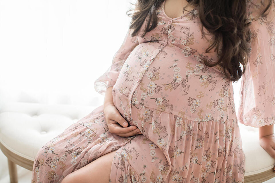 closeup of pregnant belly in pink floral dress for maternity photos