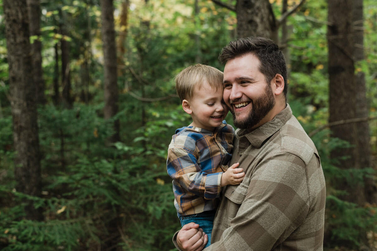 Father holding son in the forest while smiling.