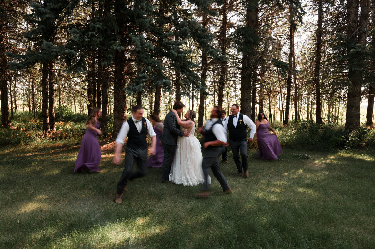 bride and groom standing in the middle of photo still, looking at each other while the wedding party runs around them creating motion blur for an artistic wedding portrait
