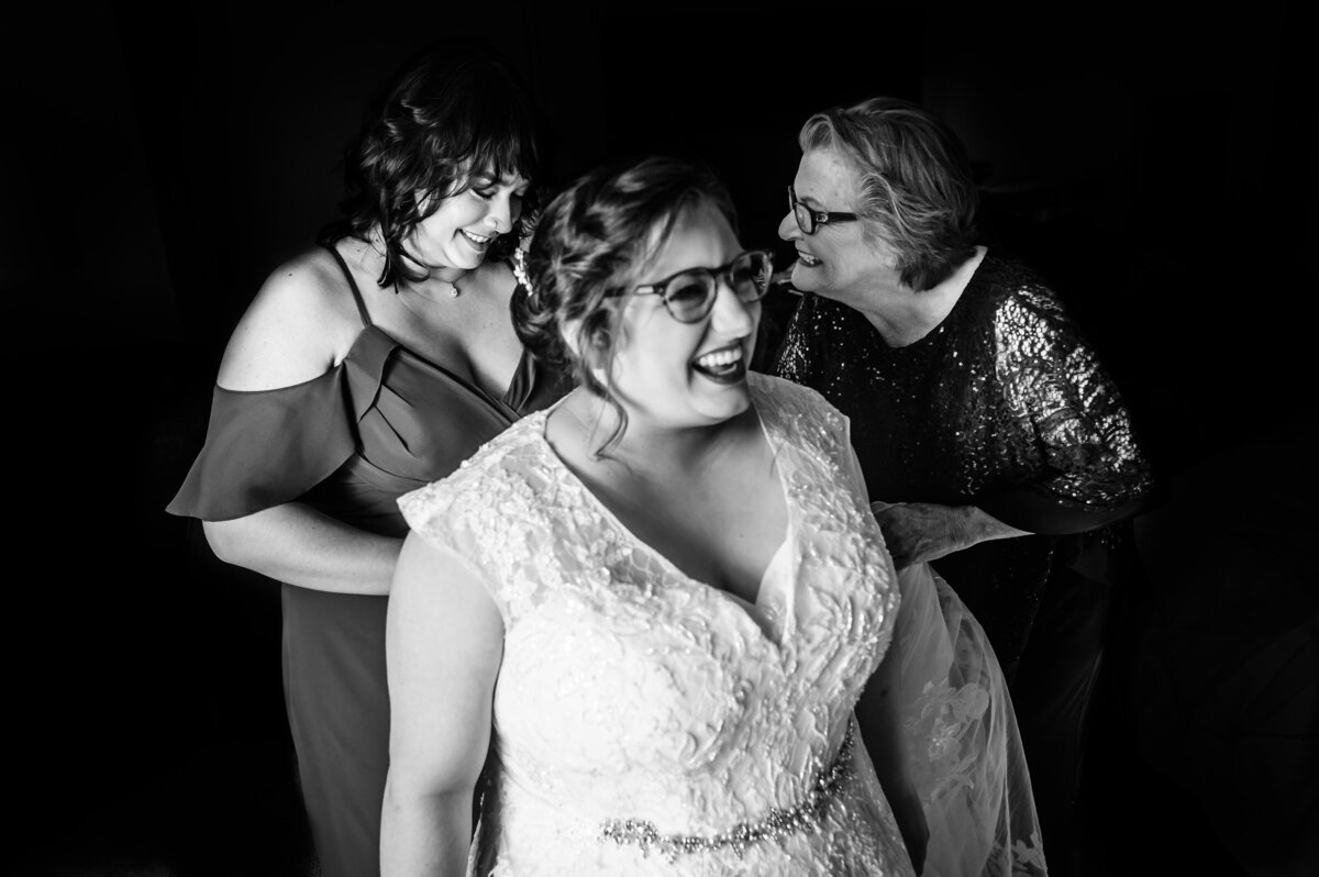 A bride smiles as the ladies helping her get ready laugh in the background
