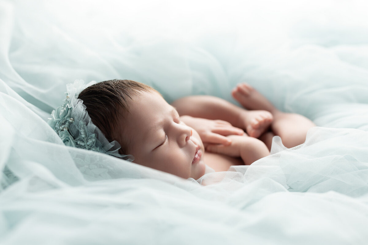 Close-up of newborn baby girl peacefully sleeping, wrapped in soft blue tulle by Dallas newborn photographer.