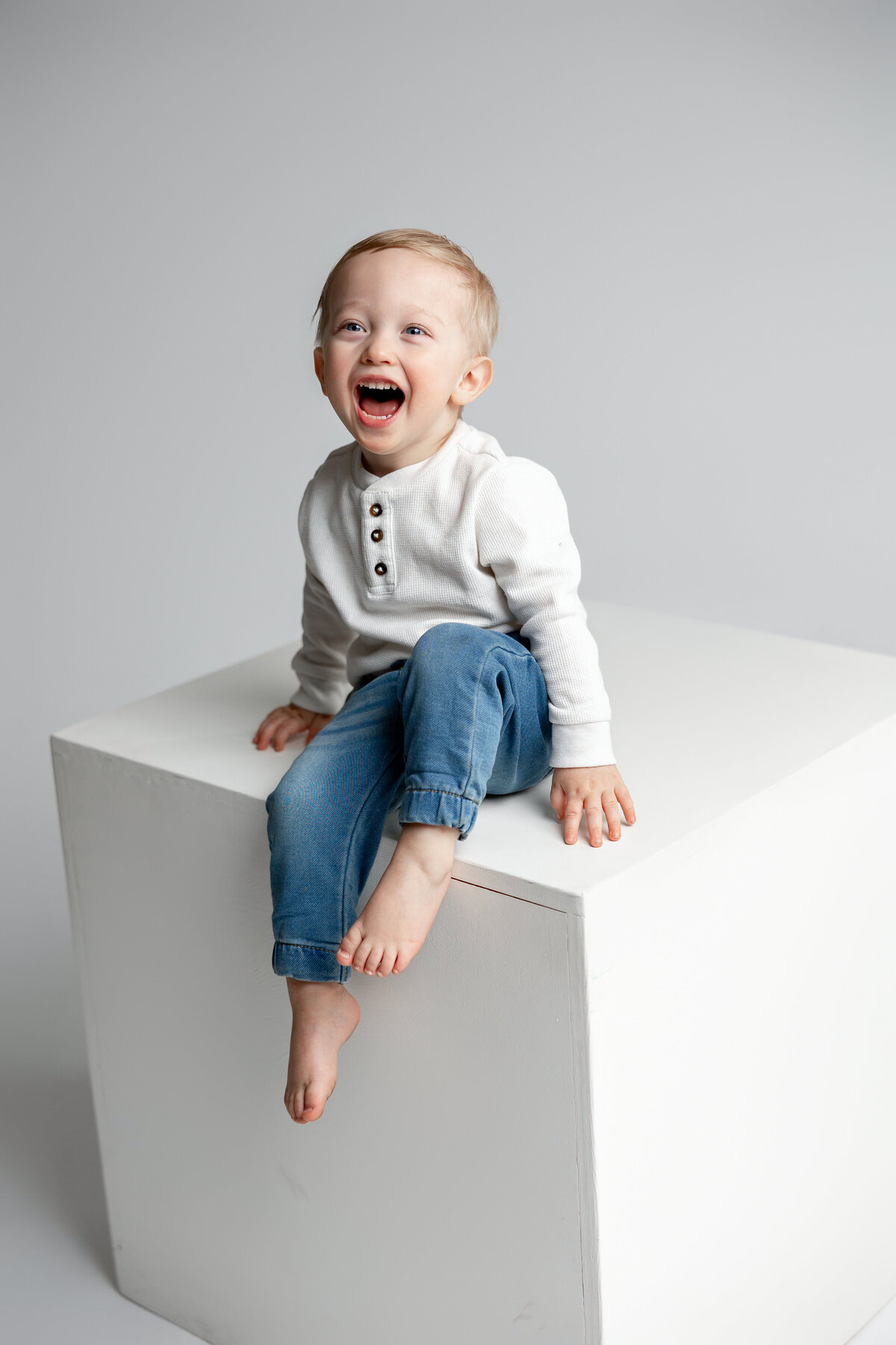 Little boy standing on cube in simple neutral outfit, looking toward camera. Photographed by Yucaipa family photographer Kaitlyn Dawn Photography