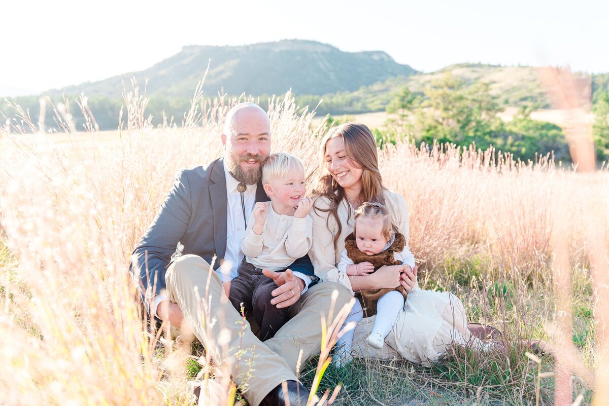 A young couple sits in a field in front of the castle rock mountains near dawson butte open space captured by denver family photographer